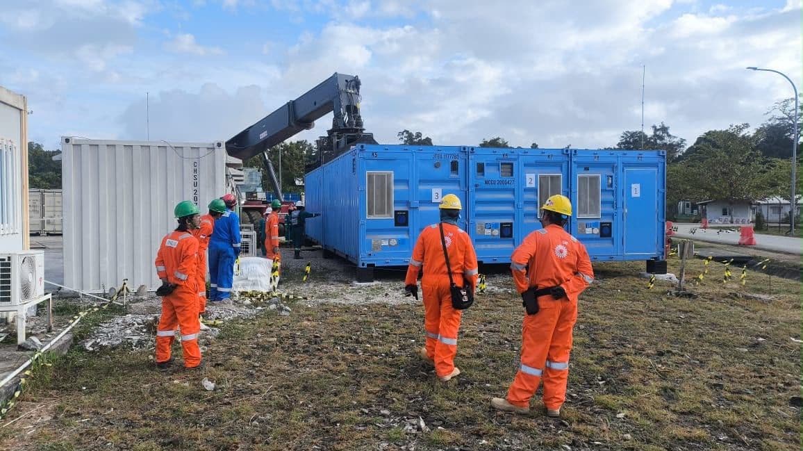 Crane menurunkan container, pekerja memakai seragam oranye